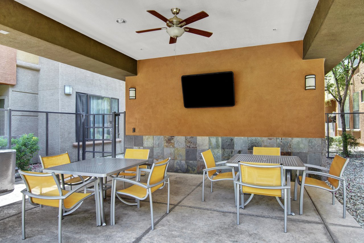 Covered outdoor seating area with tables, chairs, ceiling fan, and TV.