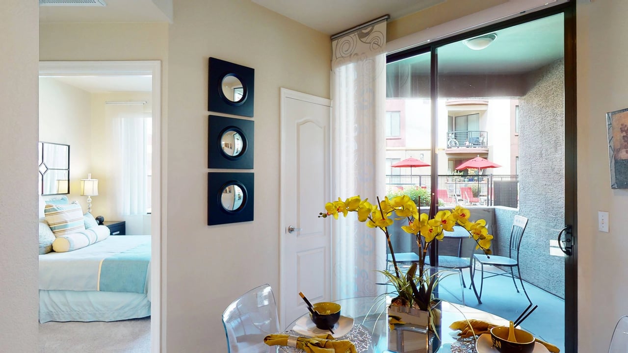 Dining area with a glass table and chairs, opening to a bedroom and a balcony.
