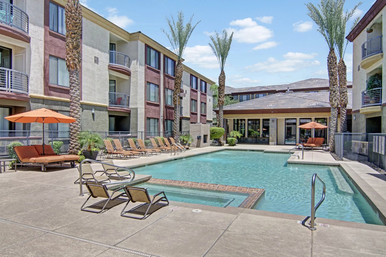 Resort-style swimming pool with lounge chairs and umbrellas at an apartment complex.