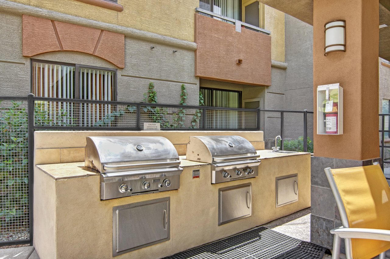 Outdoor grilling station with two large stainless steel grills and a sink, next to a residential building.