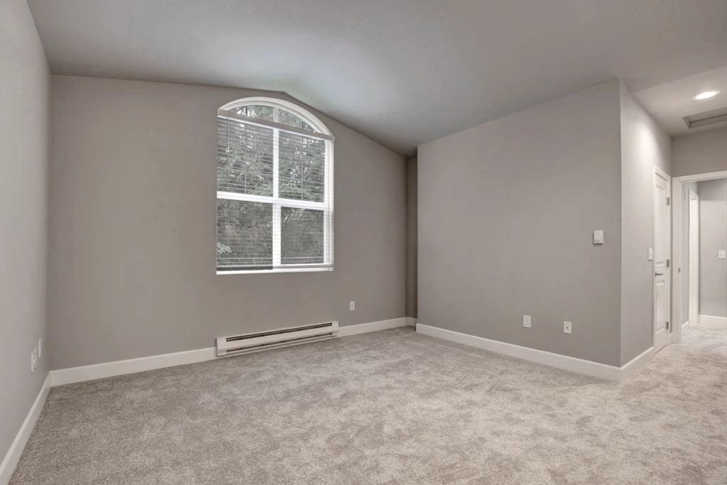 Empty apartment living room with neutral walls, carpet, and a large arched window.