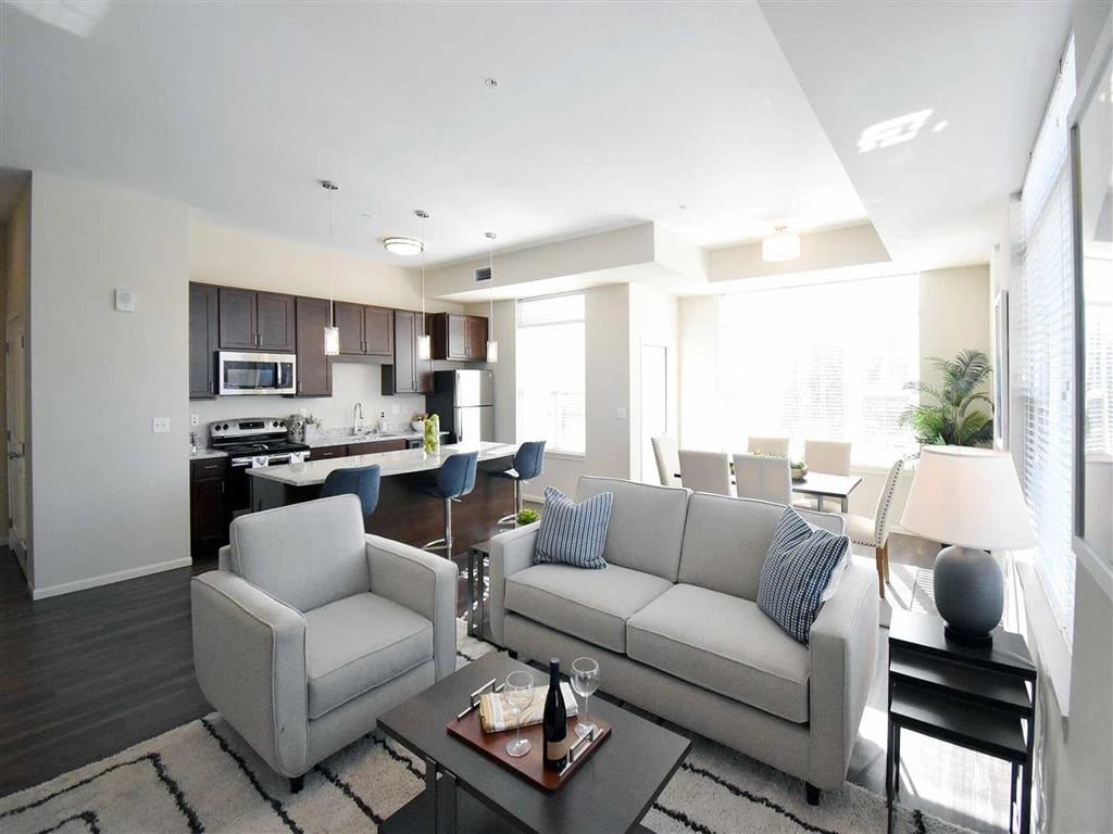Modern living room and kitchen with gray sofa, armchair, kitchen island with bar stools, and dining area.
