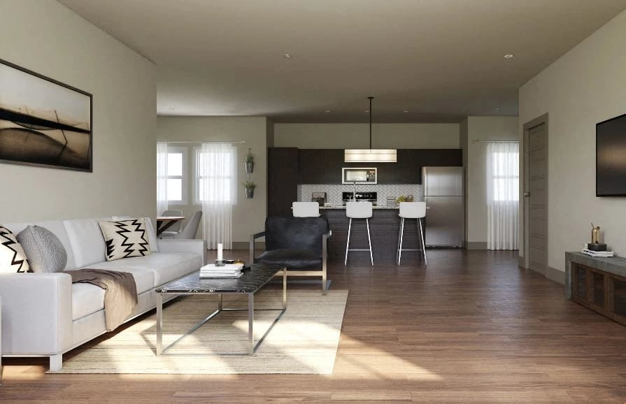 Open concept living room and kitchen with white sofa, modern kitchen island with bar stools, and stainless steel appliances.