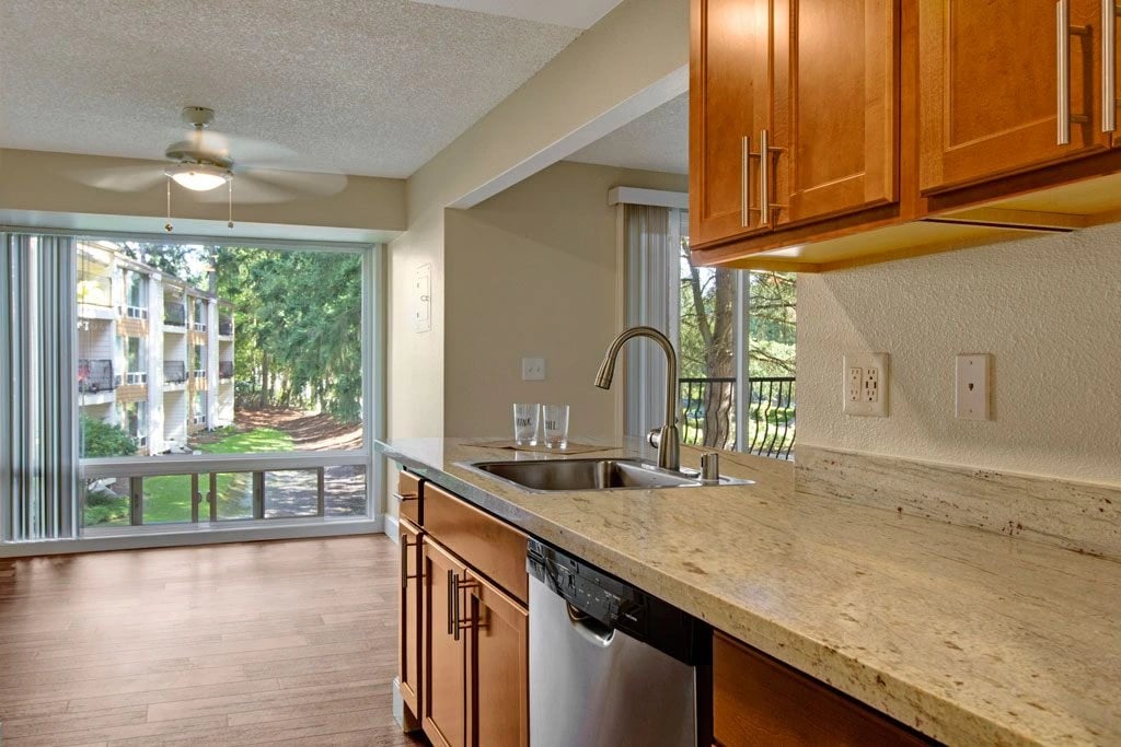 Modern kitchen with granite countertops, stainless steel appliances, and a large window with a view of the exterior.