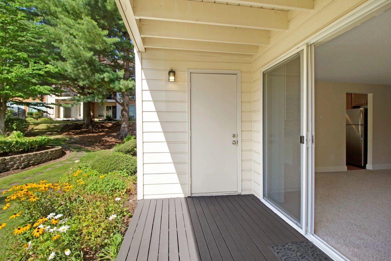 Private patio with a door leading to the apartment interior, overlooking a green courtyard with flowers.