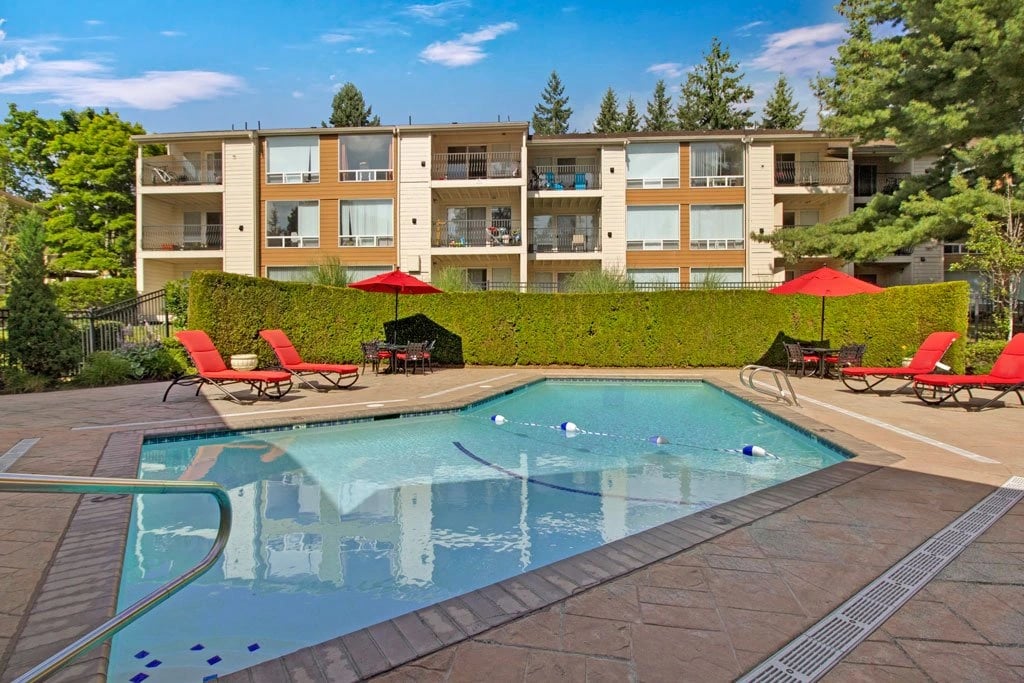 Swimming pool with lounge chairs and tables outside an apartment building.