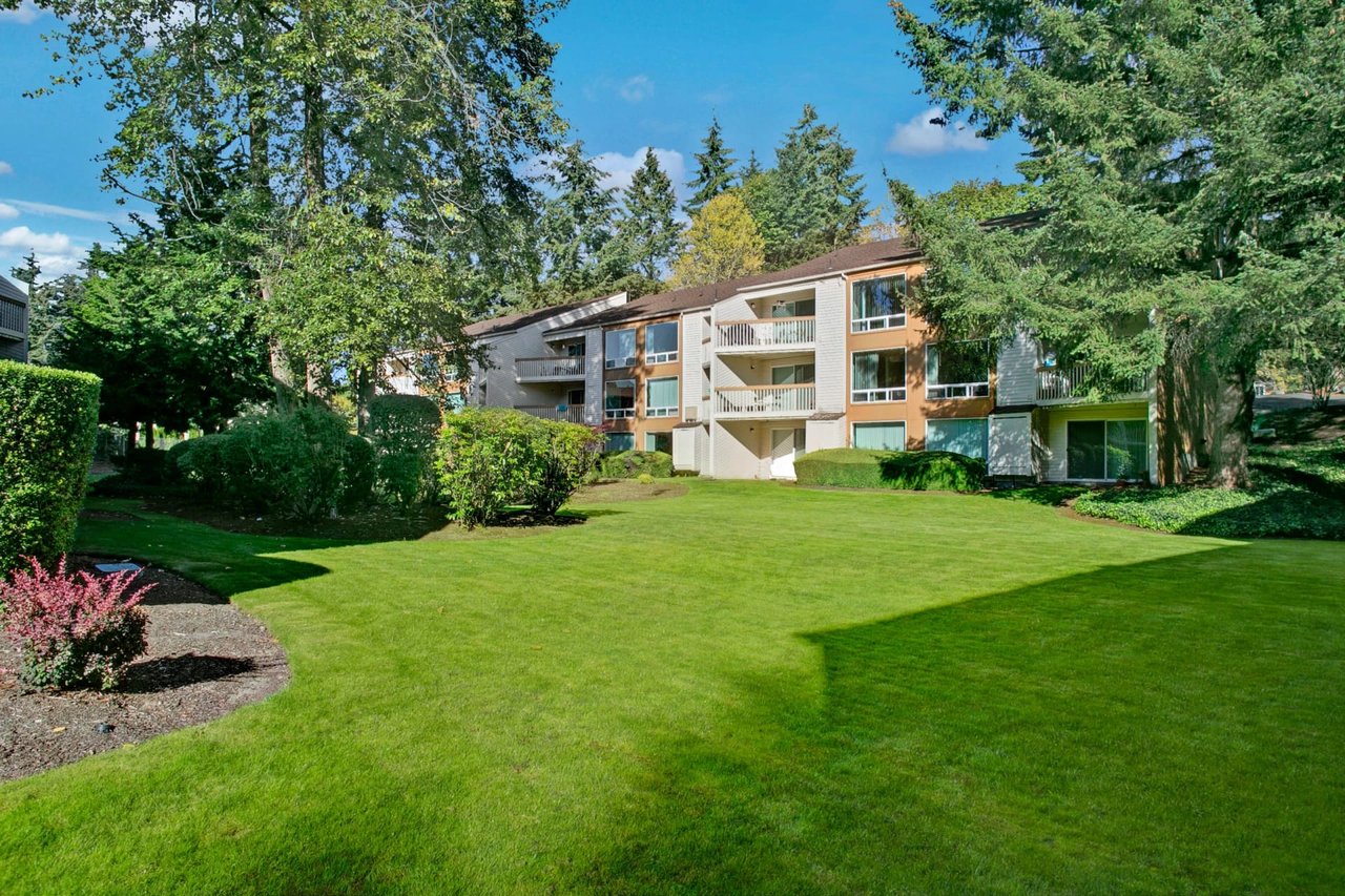 Exterior view of apartment buildings with manicured lawns and mature trees.