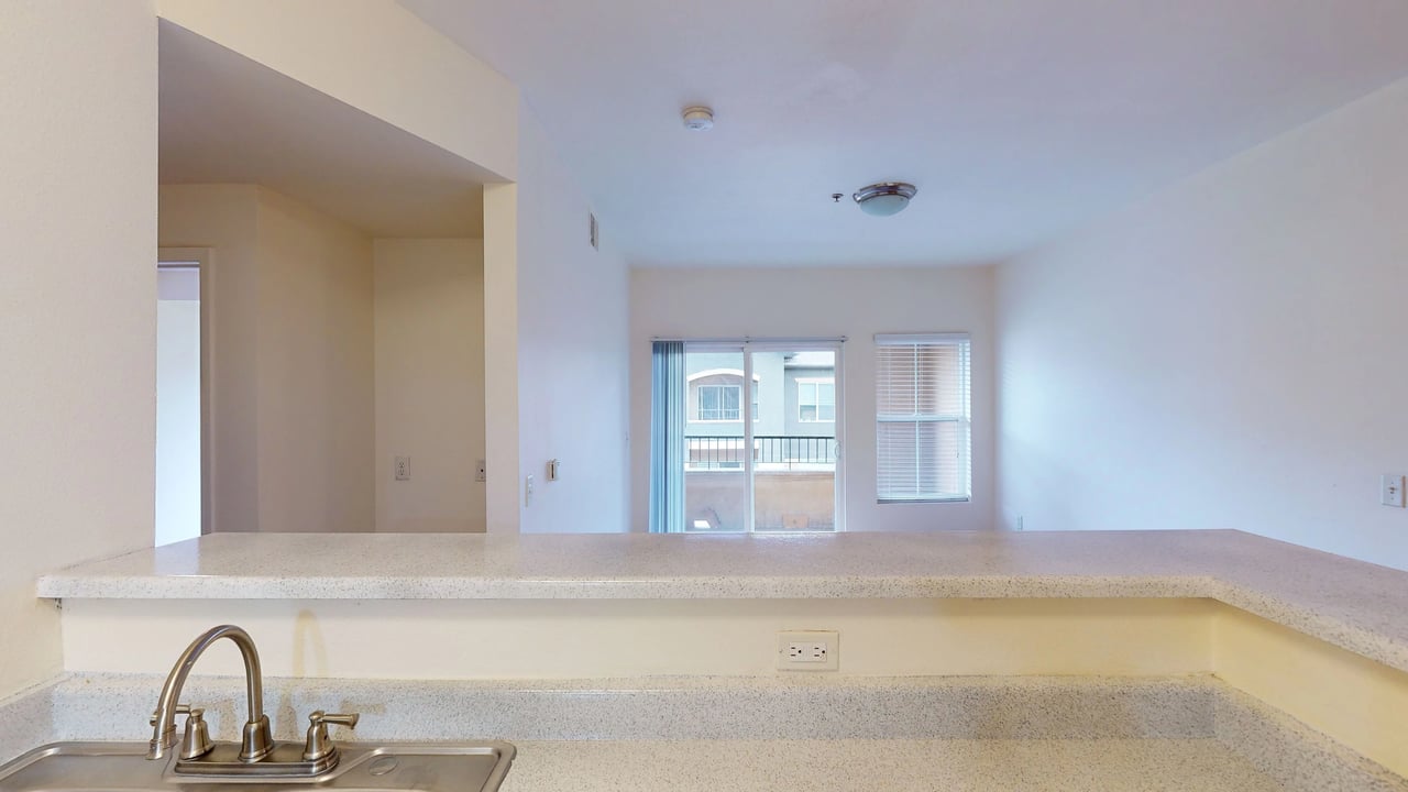 Kitchen island with sink and faucet, looking into living area with balcony access.