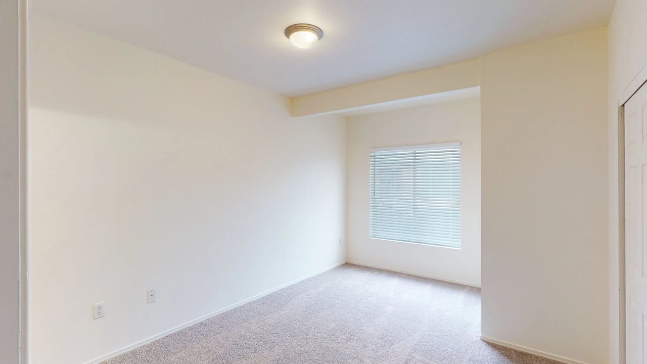 Empty bedroom with carpet, window with blinds, and light fixture.