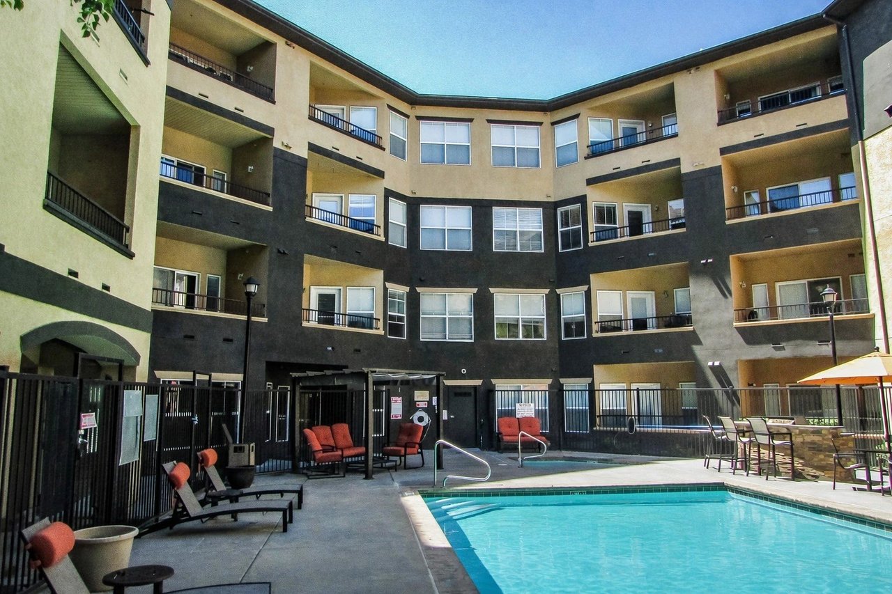 Apartment building exterior with a swimming pool and lounge chairs.