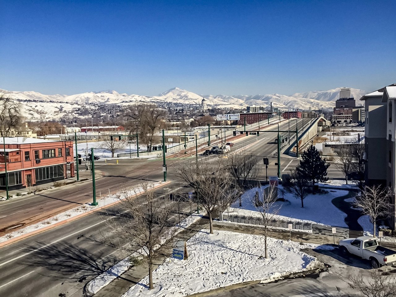View of a city street with snow on the ground and mountains in the background.