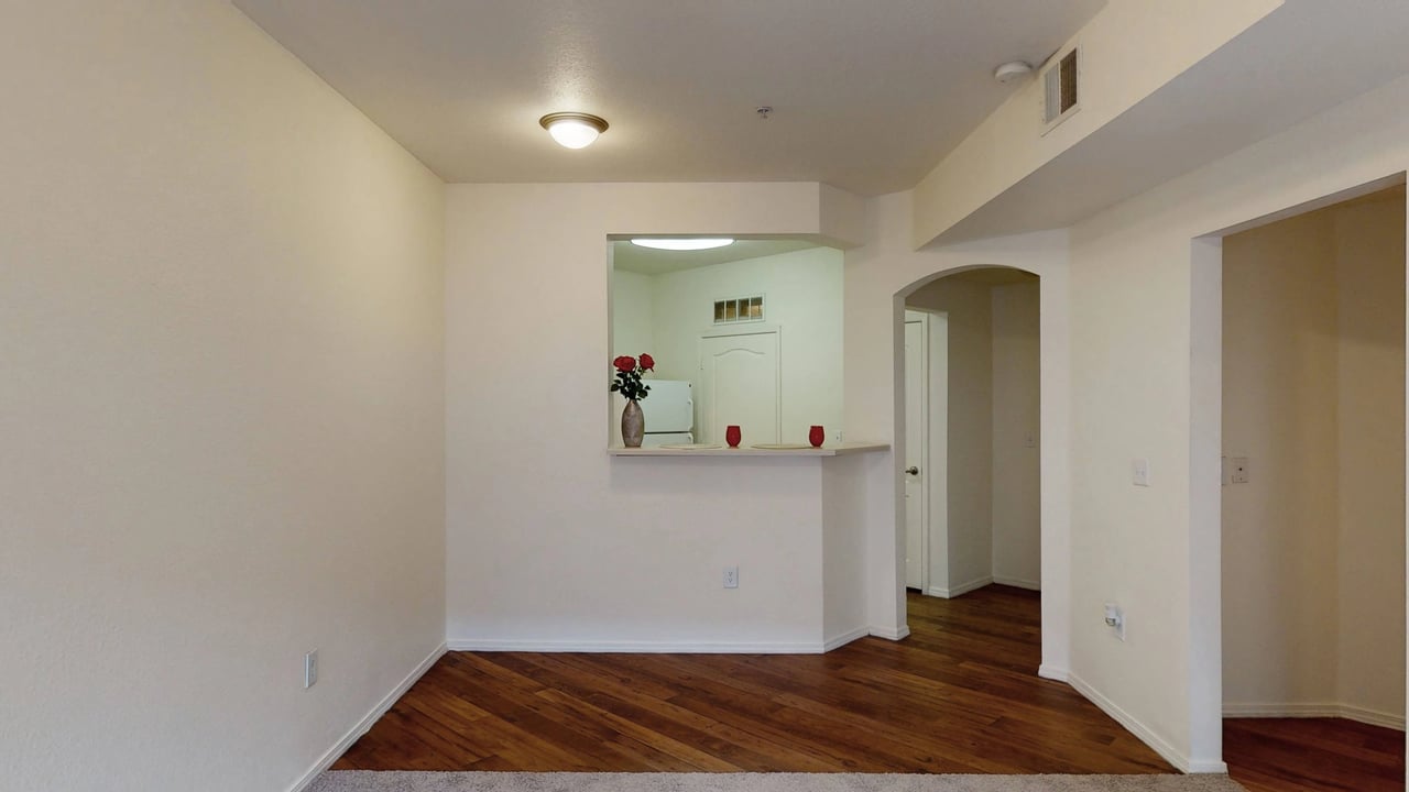 Interior view of an apartment with an open kitchen pass-through and hardwood floors.