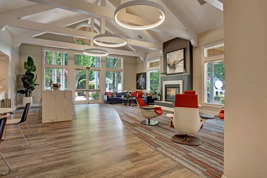 Spacious community lounge with fireplace, modern seating, and large windows overlooking greenery.