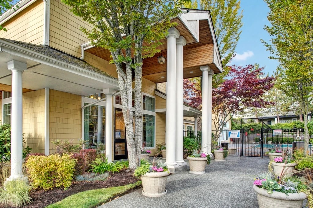 Apartment building entrance with columns and potted plants, leading to a pool area.