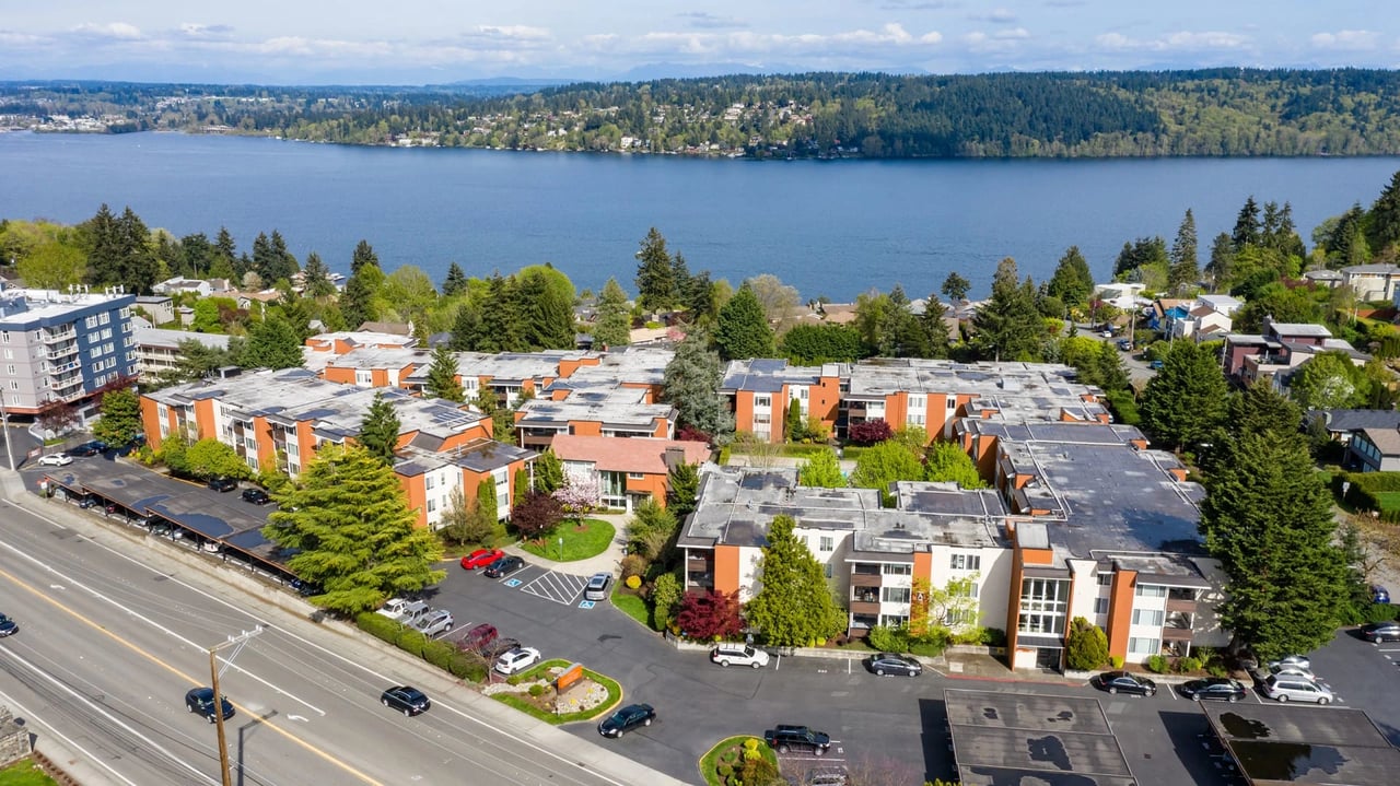 Aerial view of an apartment complex with a lake and forest in the background.