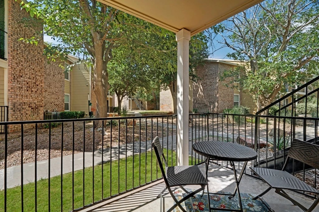 Balcony with a small table and chairs overlooking a courtyard with trees and apartment buildings.