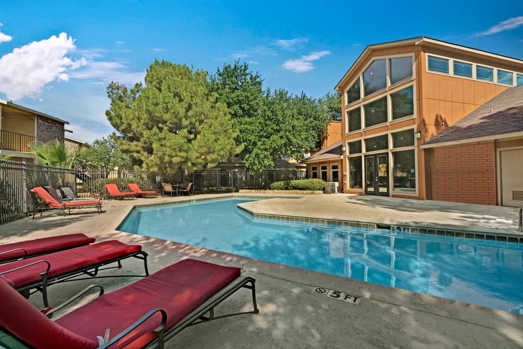 Resort-style swimming pool with lounge chairs and a building in the background.