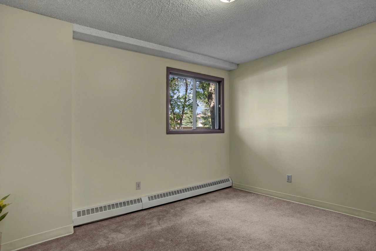A vacant bedroom with a single window overlooking trees.