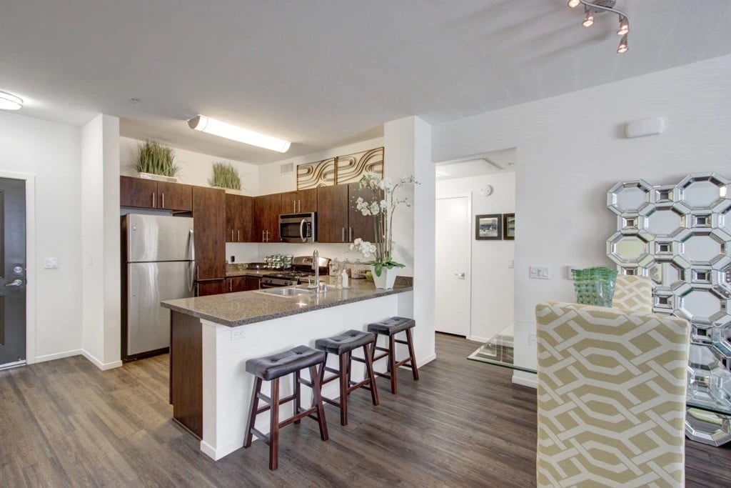 Modern kitchen with dark wood cabinets, granite countertops, stainless steel appliances, and a breakfast bar with stools.
