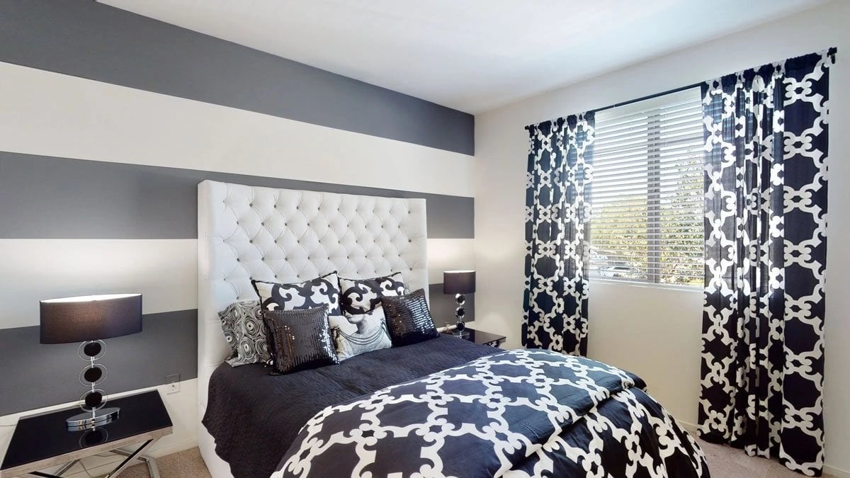 Stylish bedroom with a tufted headboard, dark bedding, and striped walls.