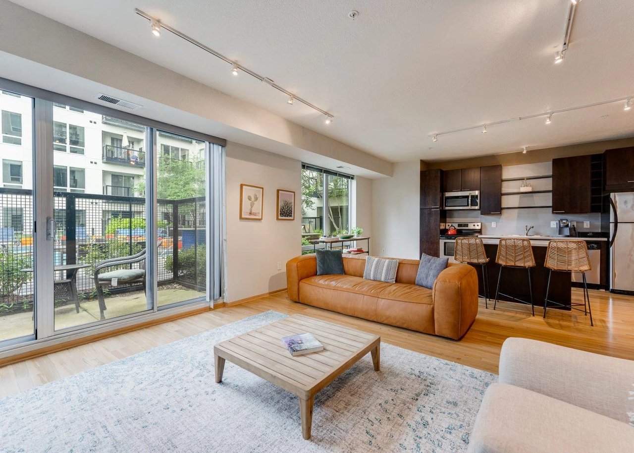 Modern living room and kitchen area with a tan sofa, coffee table, and island seating.