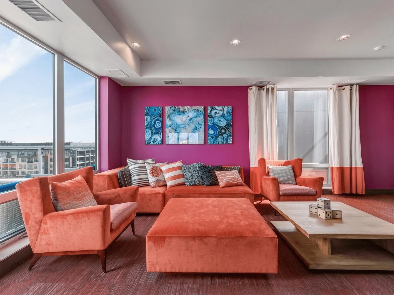 Modern communal lounge with bright orange sectional sofa, accent chairs, and artwork.