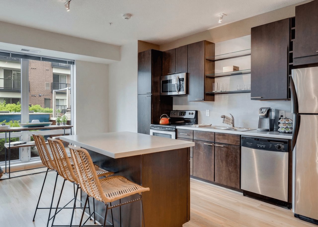 Modern kitchen with dark wood cabinets, stainless steel appliances, and a large island with bar stools.