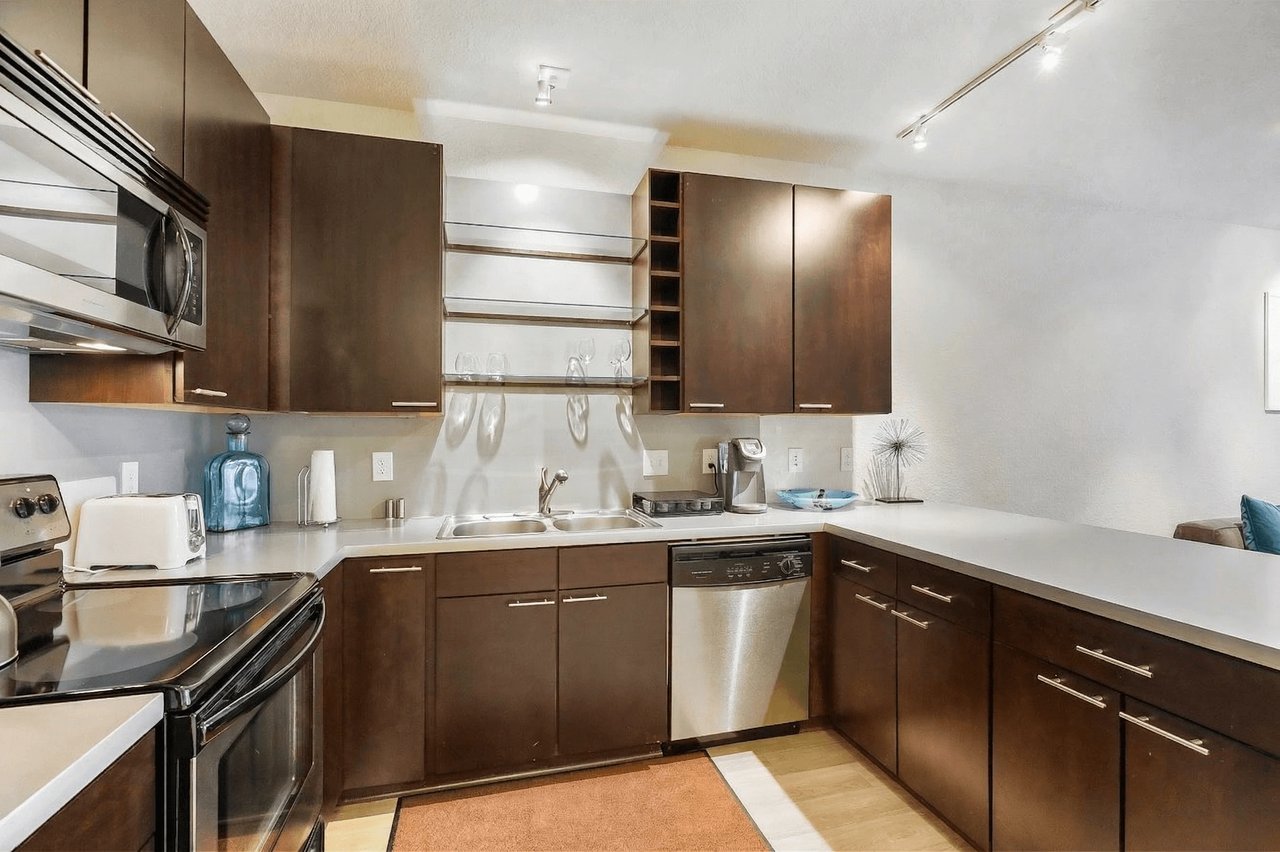Modern kitchen with dark wood cabinets, stainless steel appliances, and a large countertop.