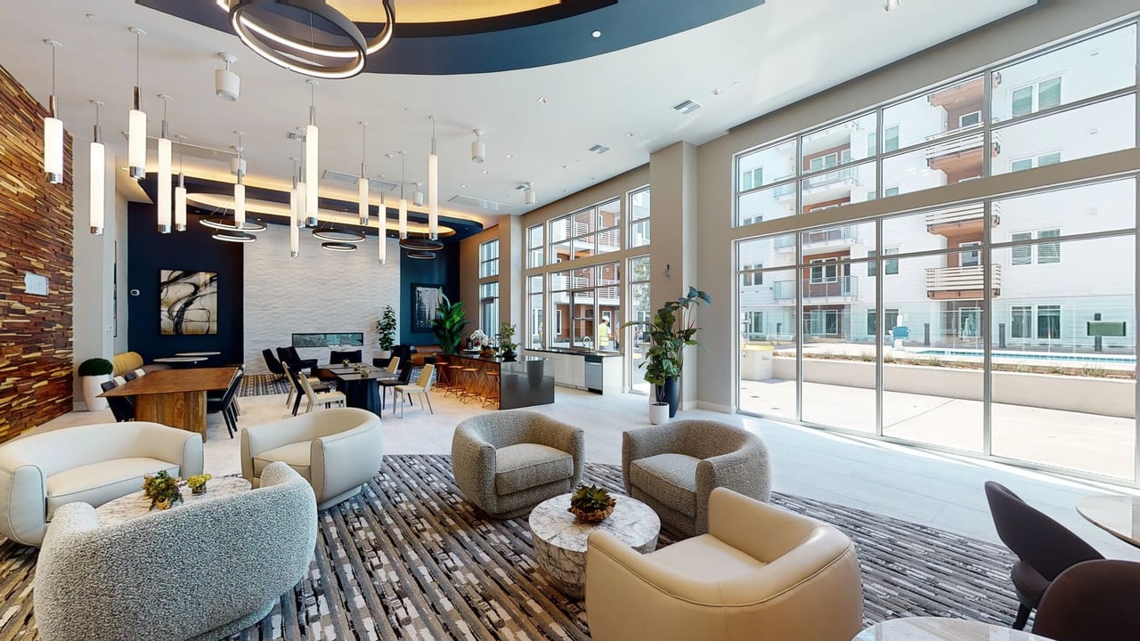 Modern apartment building lobby with comfortable seating, a fireplace, and large windows overlooking the pool.