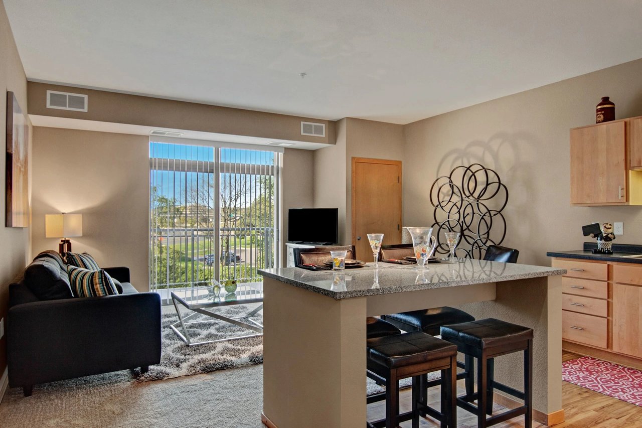 Open-plan living room with a sofa, granite kitchen island, and sliding glass door to the balcony.