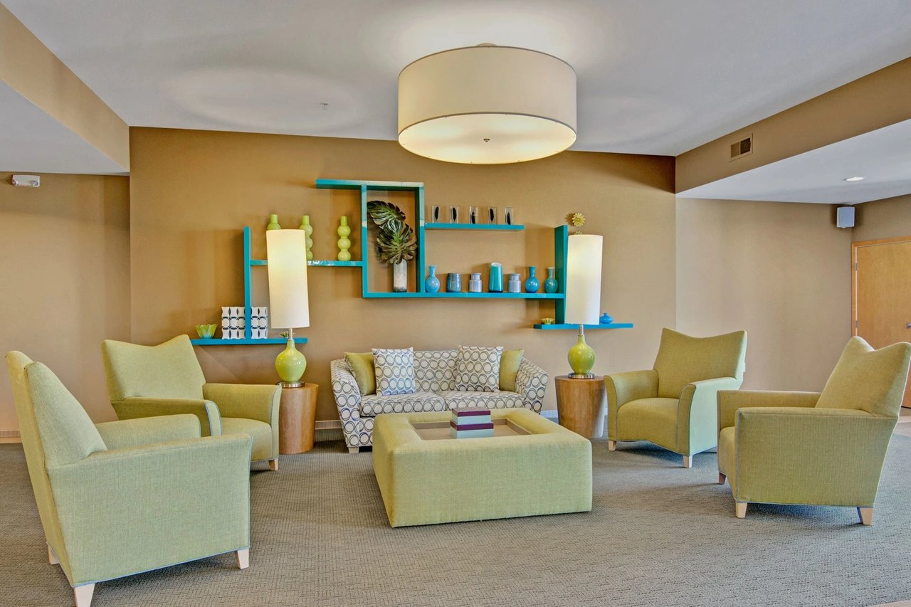 Indoor resident lounge with lime-green chairs, a patterned sofa, and blue wall shelving.