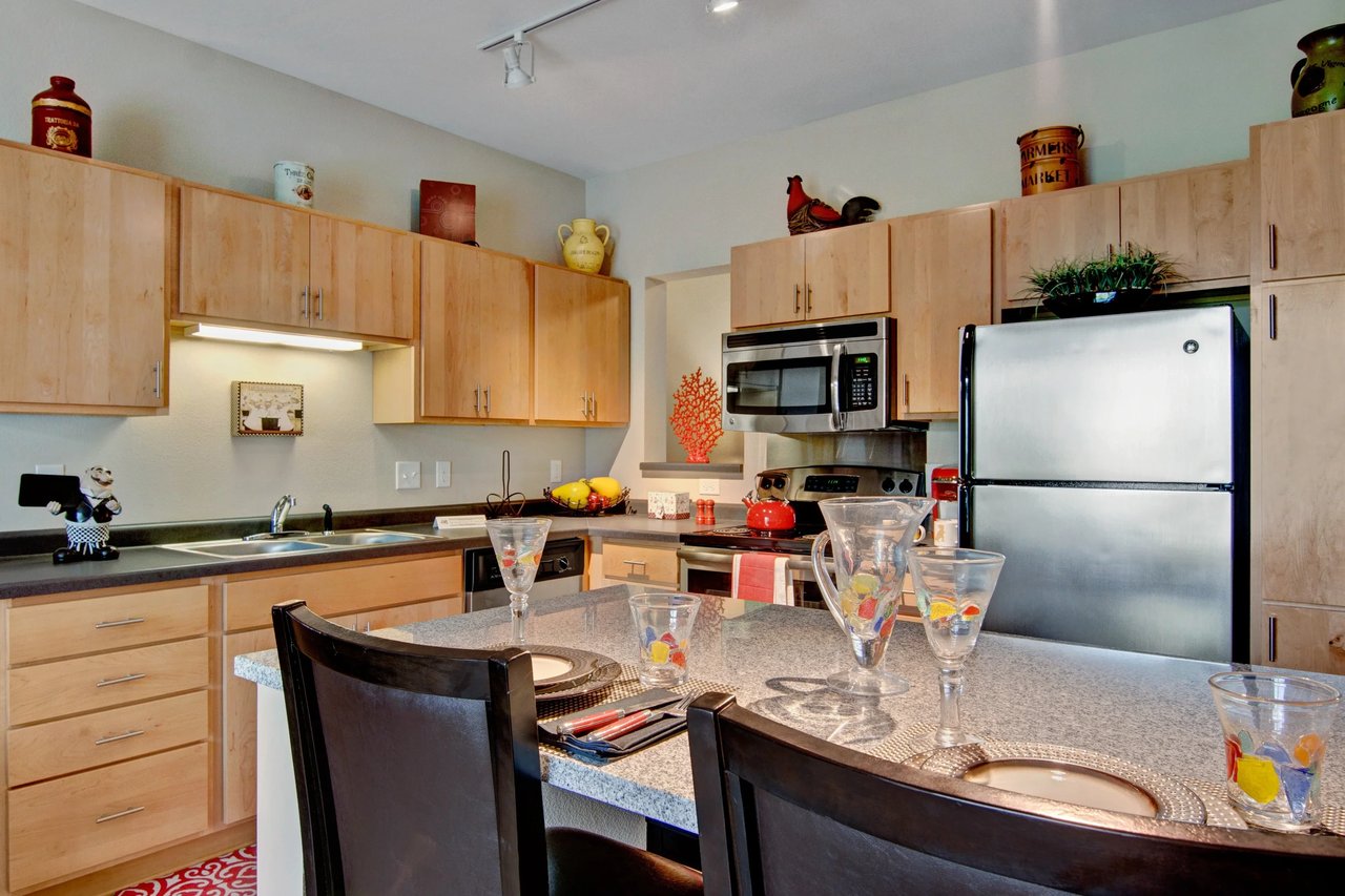 Bright apartment kitchen with light wood cabinets, stainless steel fridge and microwave, and island.