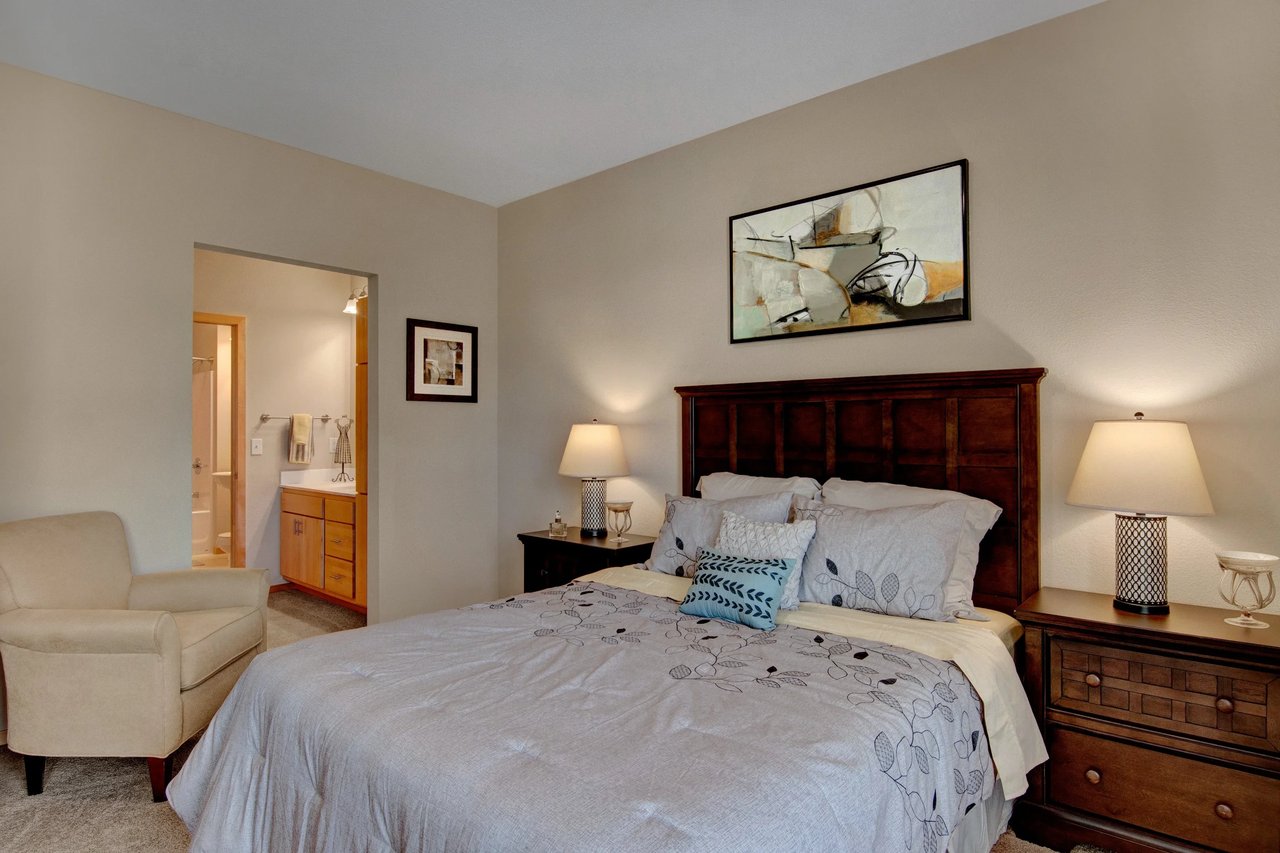 Furnished bedroom in an apartment with a wooden headboard, two nightstands, lamps, and wall art.