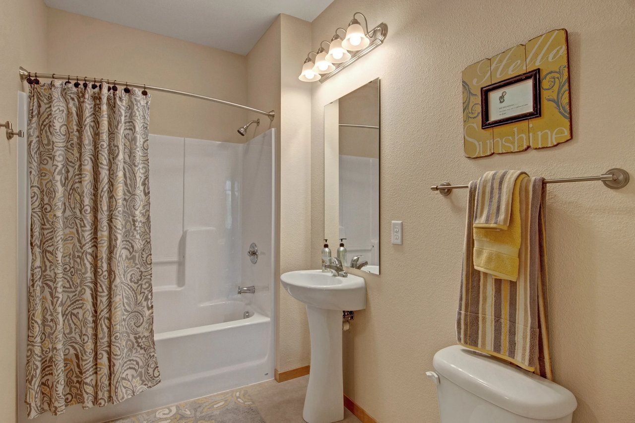 Bathroom in apartment with shower/tub, pedestal sink, mirror, and towel rack.