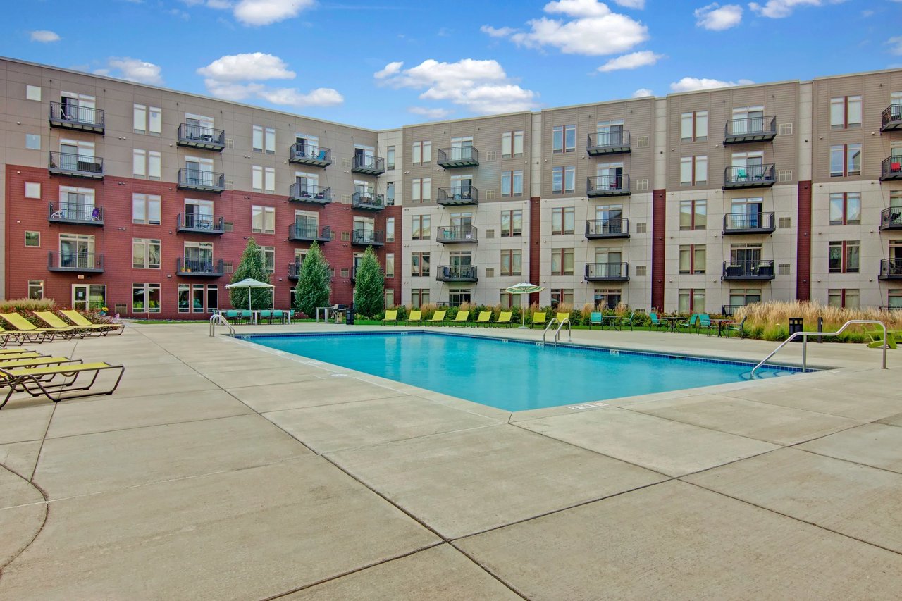 Outdoor pool area with lounge chairs and umbrellas, surrounded by a multi-story apartment building.