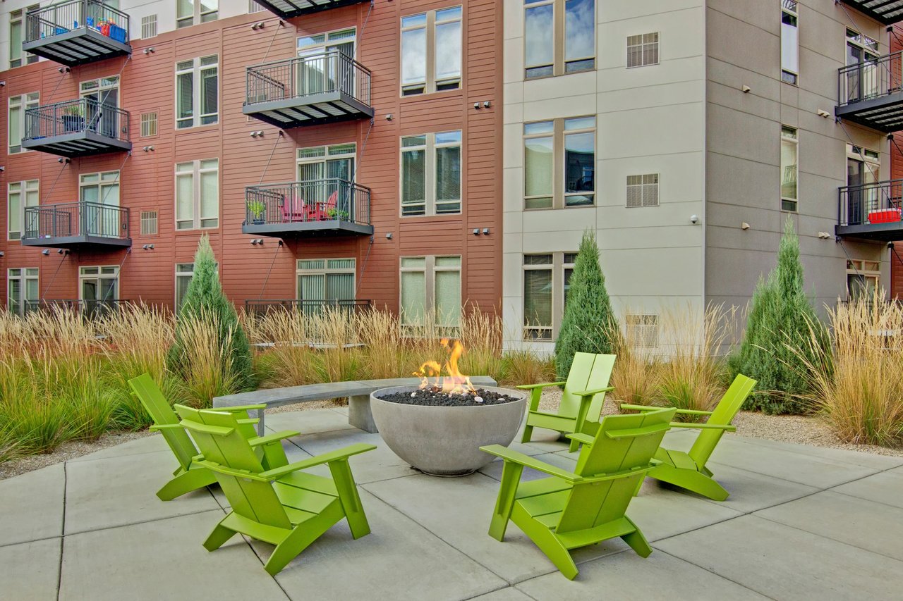 Outdoor communal courtyard with a fire pit and lime-green chairs in front of an apartment building.
