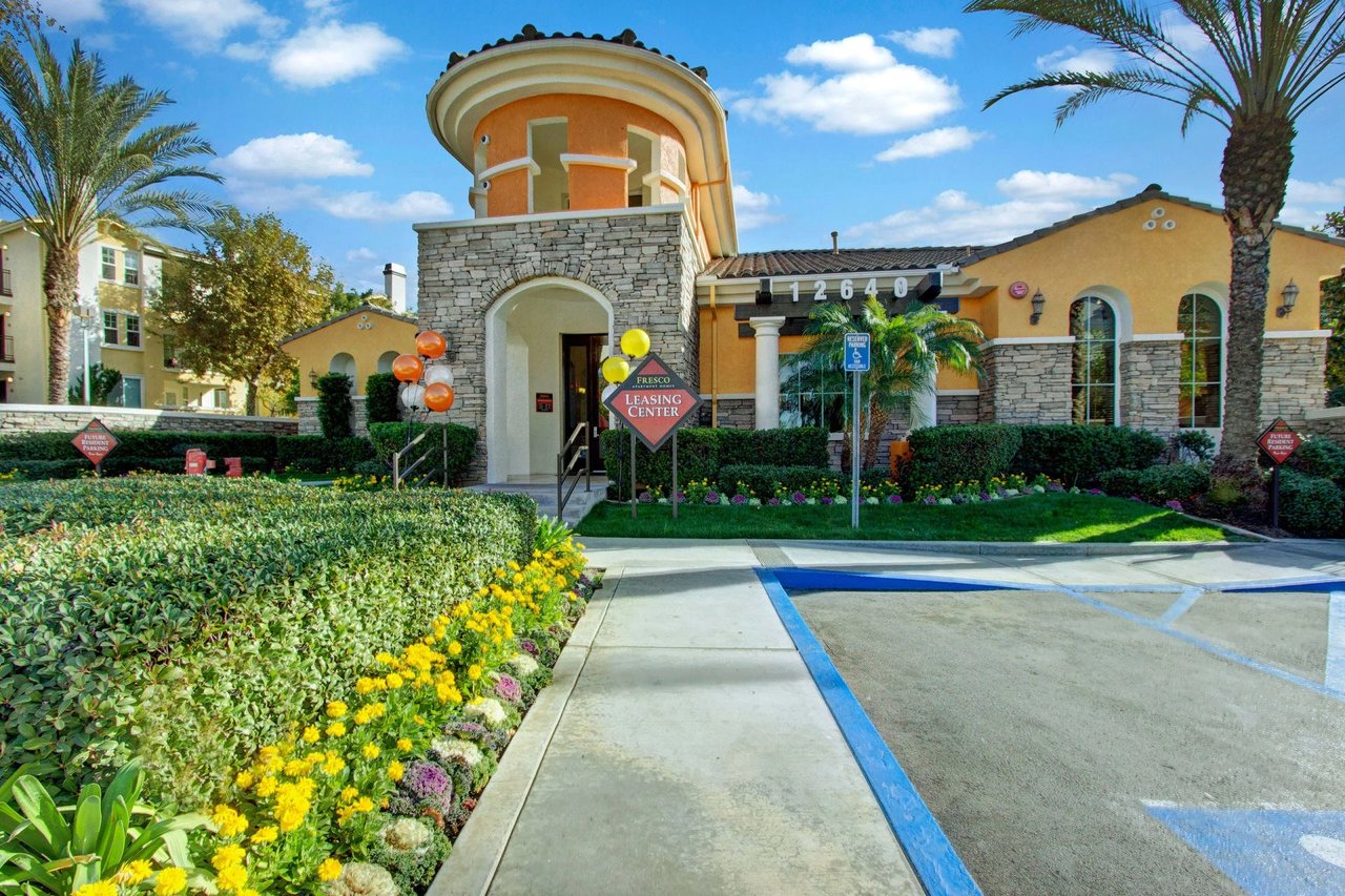 Exterior view of the Frisco Apartment Homes leasing center entrance with landscaping and parking.