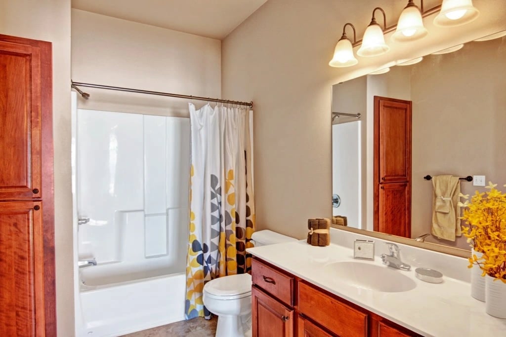 Bathroom with wood cabinets, white countertop, sink, toilet, and bathtub with shower curtain.