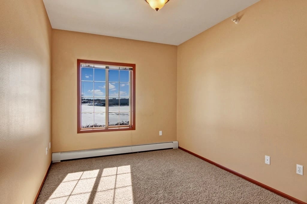 Interior view of an empty apartment room with a large window showing a snowy landscape.