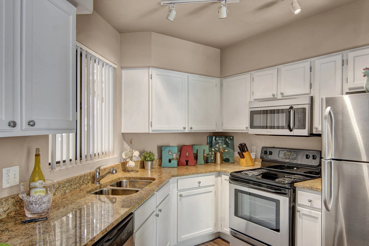 Kitchen with granite countertops, white cabinets, stainless steel appliances, and a double sink.