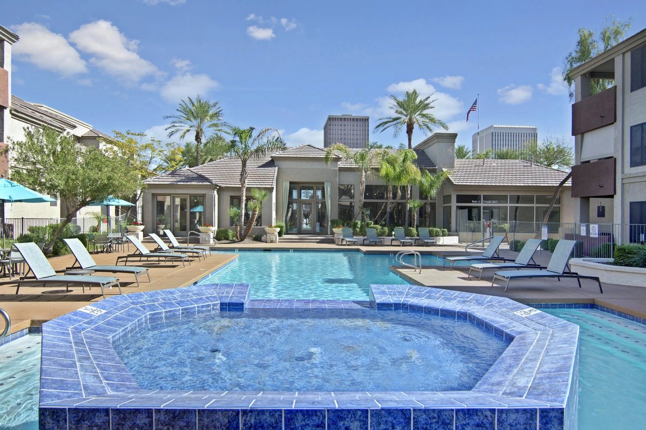 Outdoor swimming pool and hot tub area with lounge chairs and palm trees.