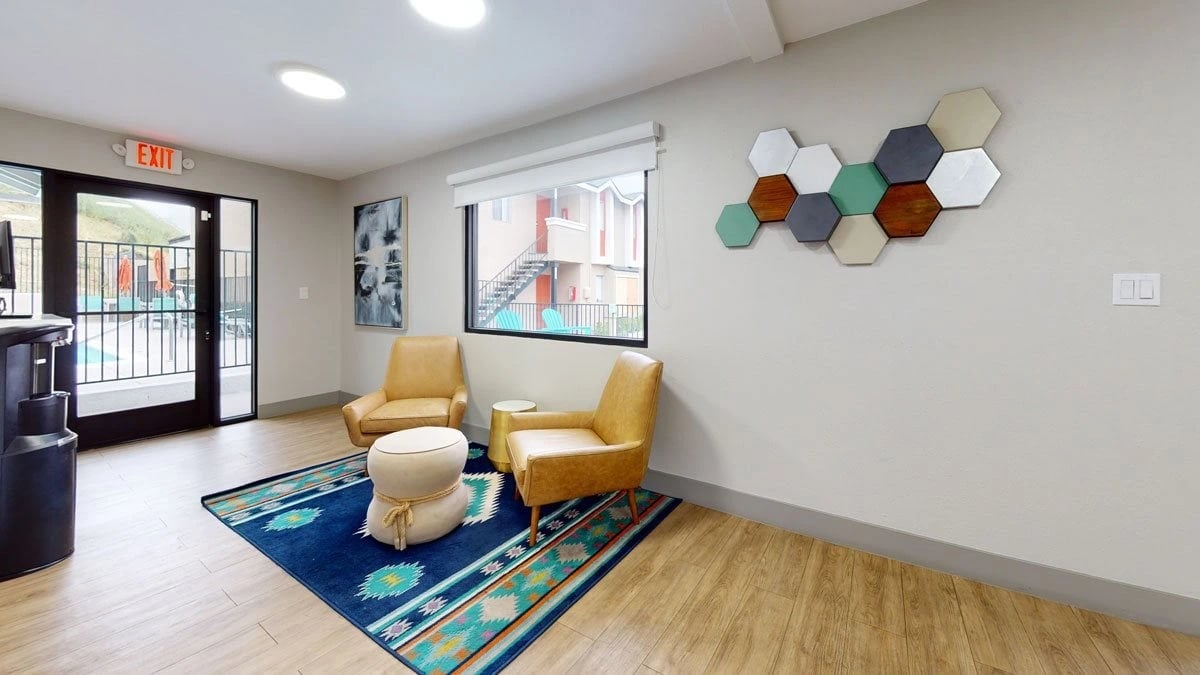 Interior lounge area with chairs and a rug, with a view of the pool area through the glass doors.