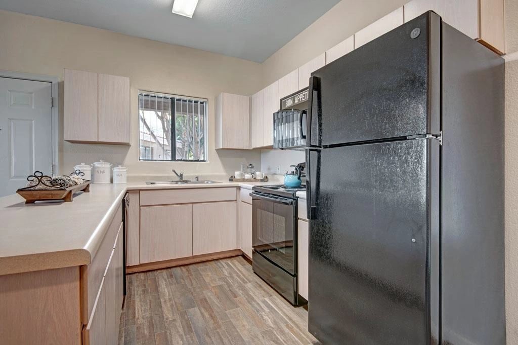 Kitchen with light wood cabinets, black appliances, and a window.