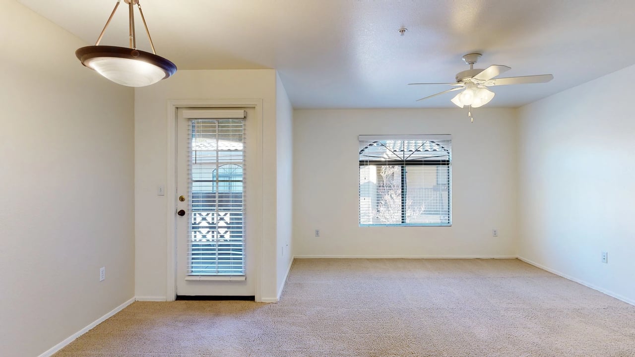 Living room with beige carpet, ceiling fan, and a door leading outside.