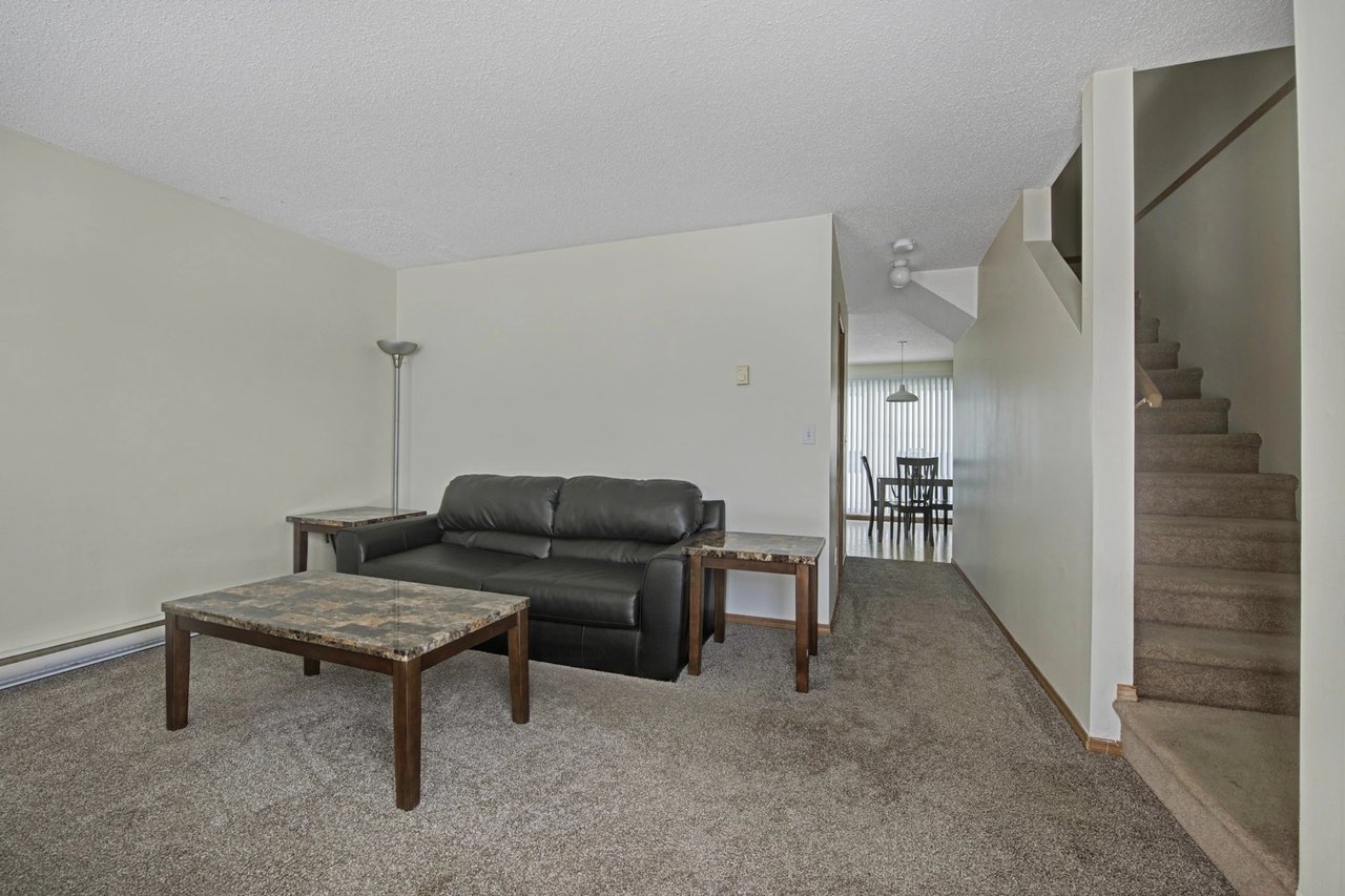 Living room with a black leather sofa, coffee table, and stairs leading upstairs.