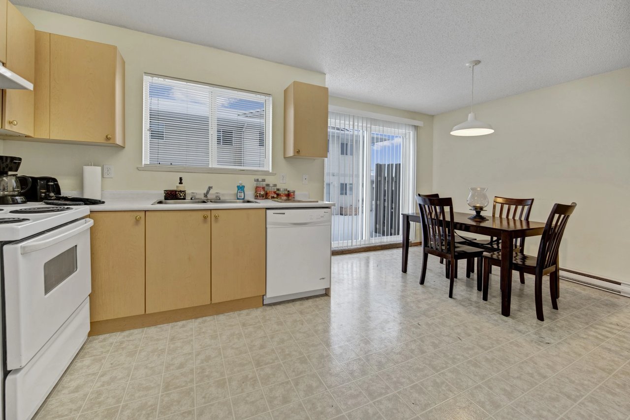 Kitchen and dining area with white appliances, light wood cabinets, and a dark wood dining table with four chairs.