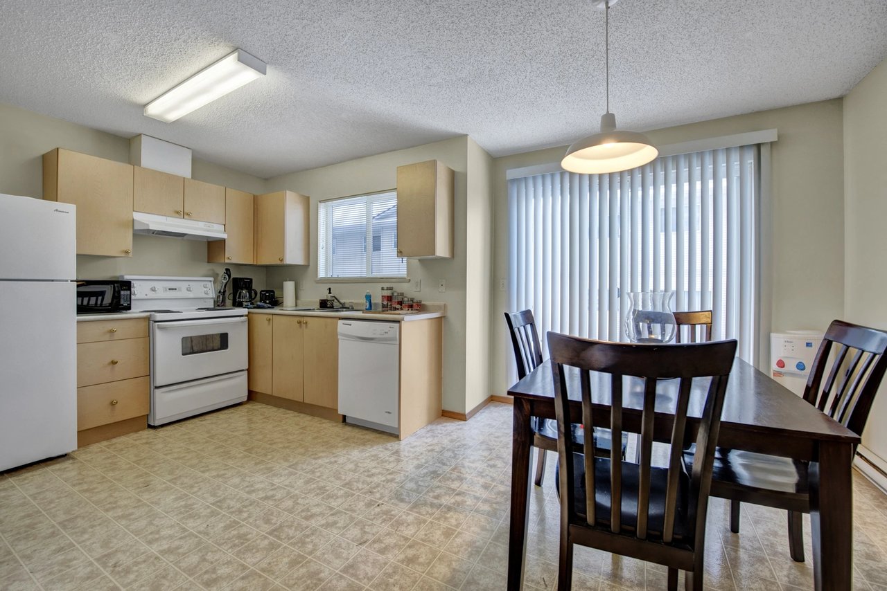 Kitchen and dining area with white appliances, light wood cabinets, and a dark wood dining table.