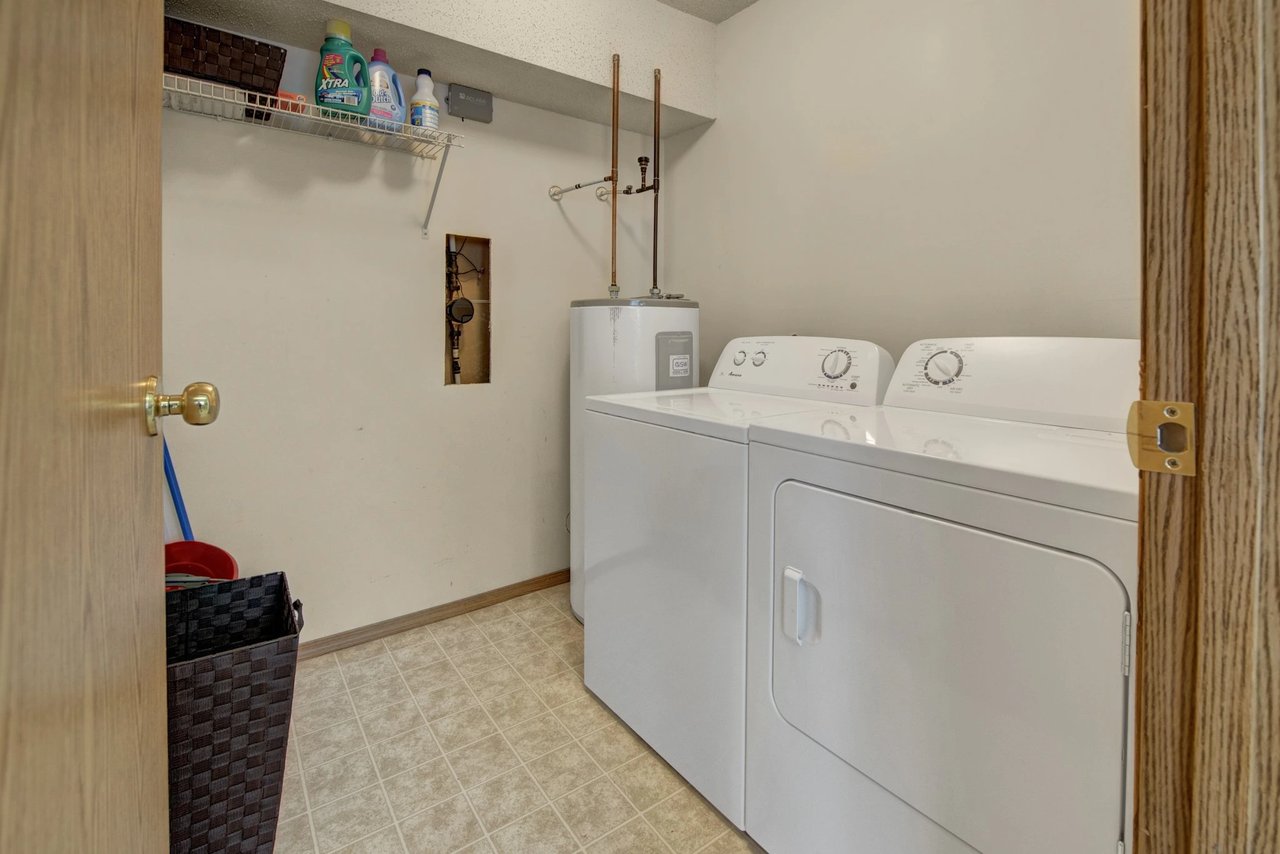 Laundry room with white washer and dryer, water heater, and shelf with cleaning supplies.