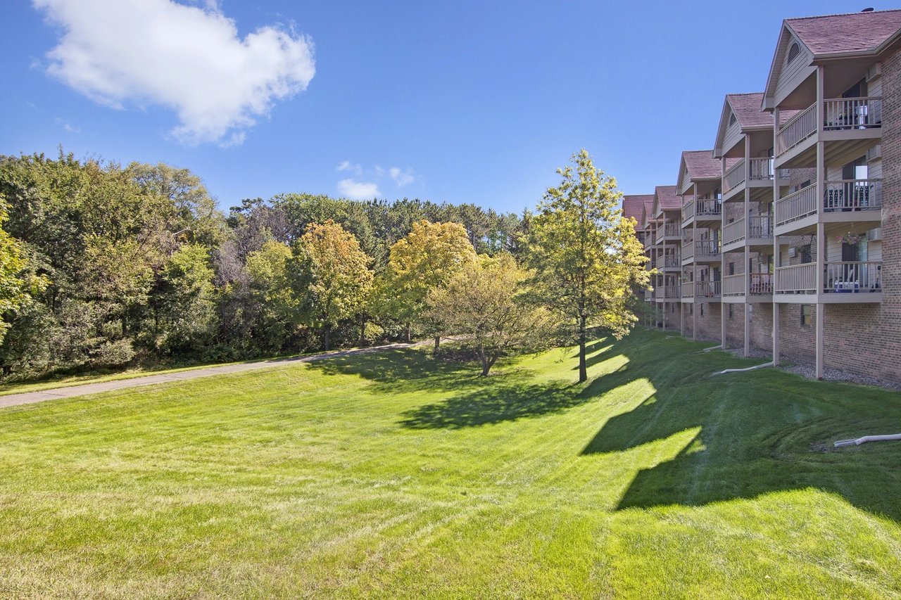 Exterior of apartment building with balconies overlooking a grassy lawn and trees.