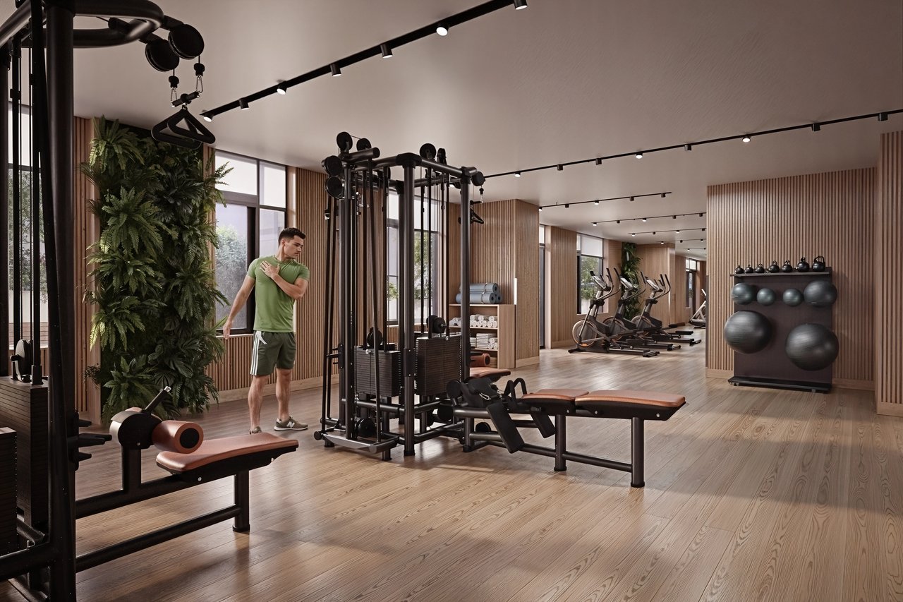 Man stretching in a modern apartment gym with cardio machines and weight training equipment.